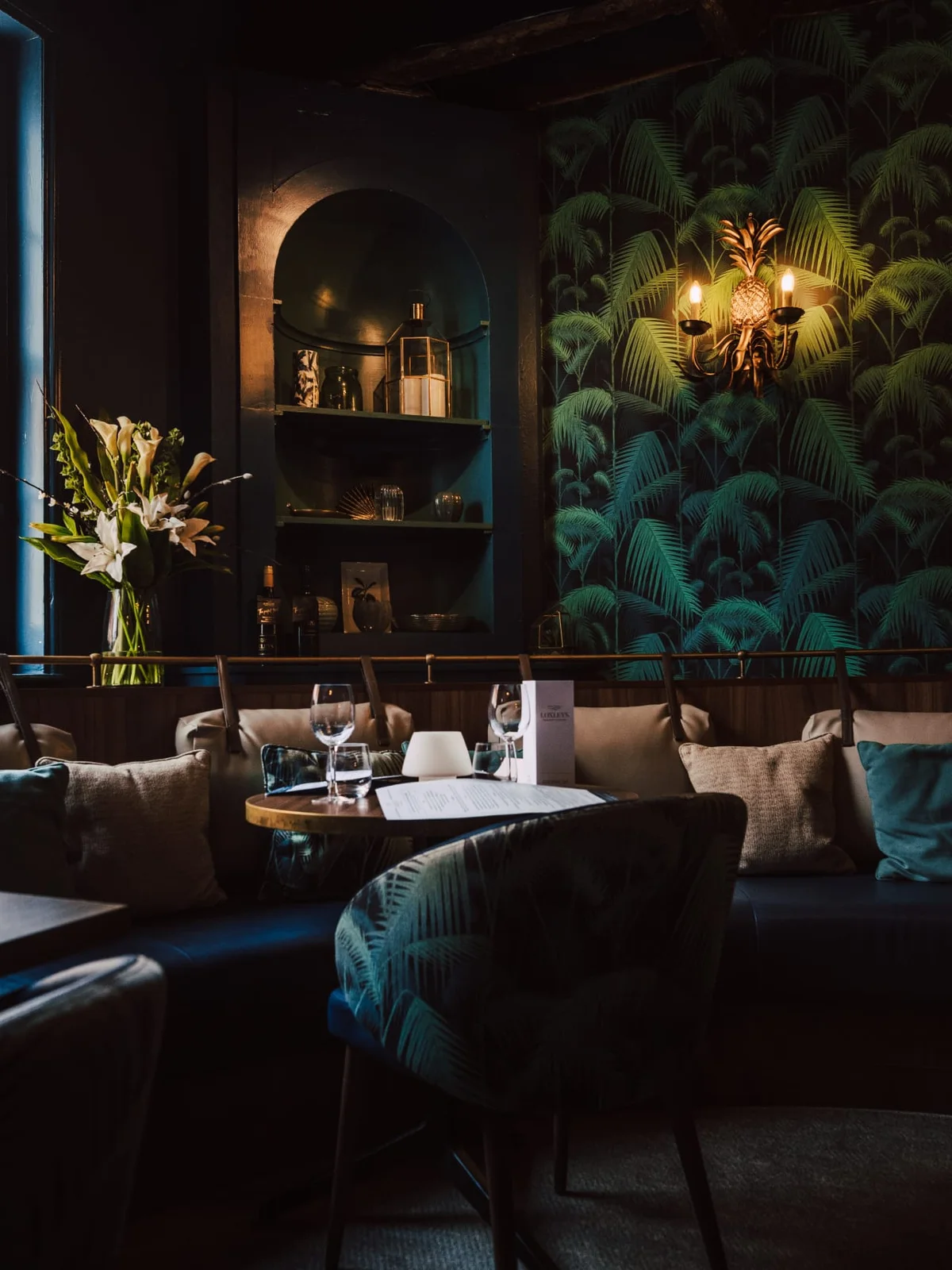 Loxleys booth with palm-print wallpaper, brass pineapple sconce and fresh flowers.