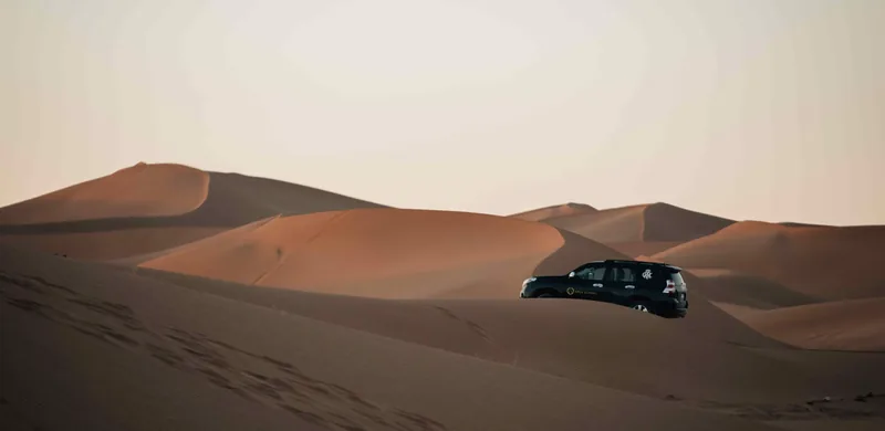 Xped Global expedition vehicle cresting a desert dune at sunset.