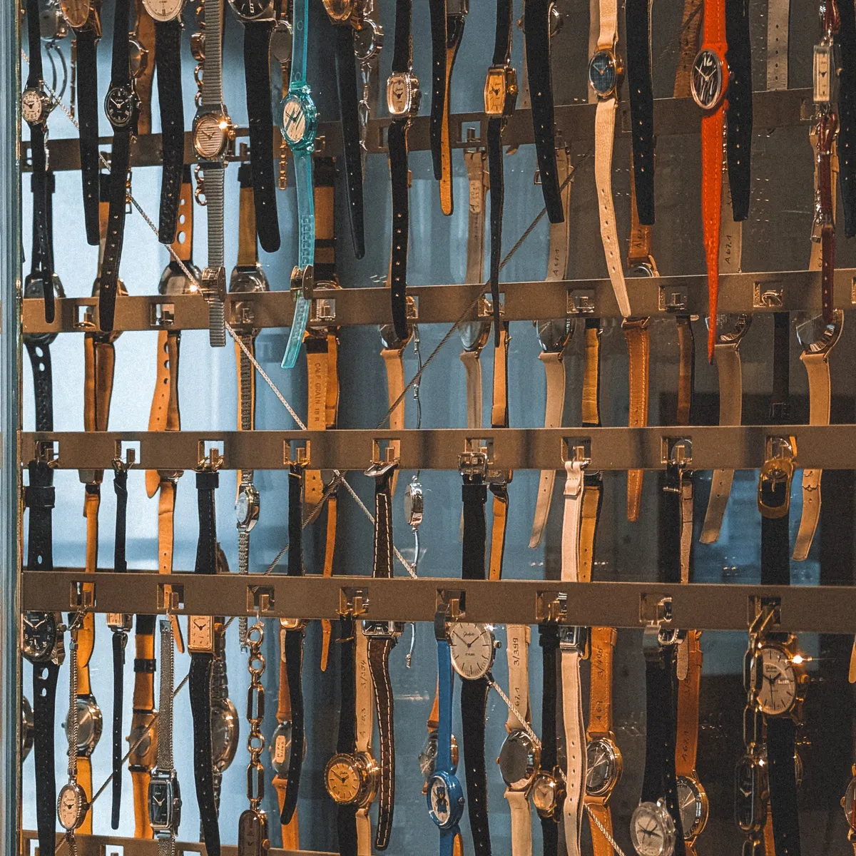 A tall glass cabinet holding rows of wristwatches on rails, dozens of different straps and dials hung side by side.